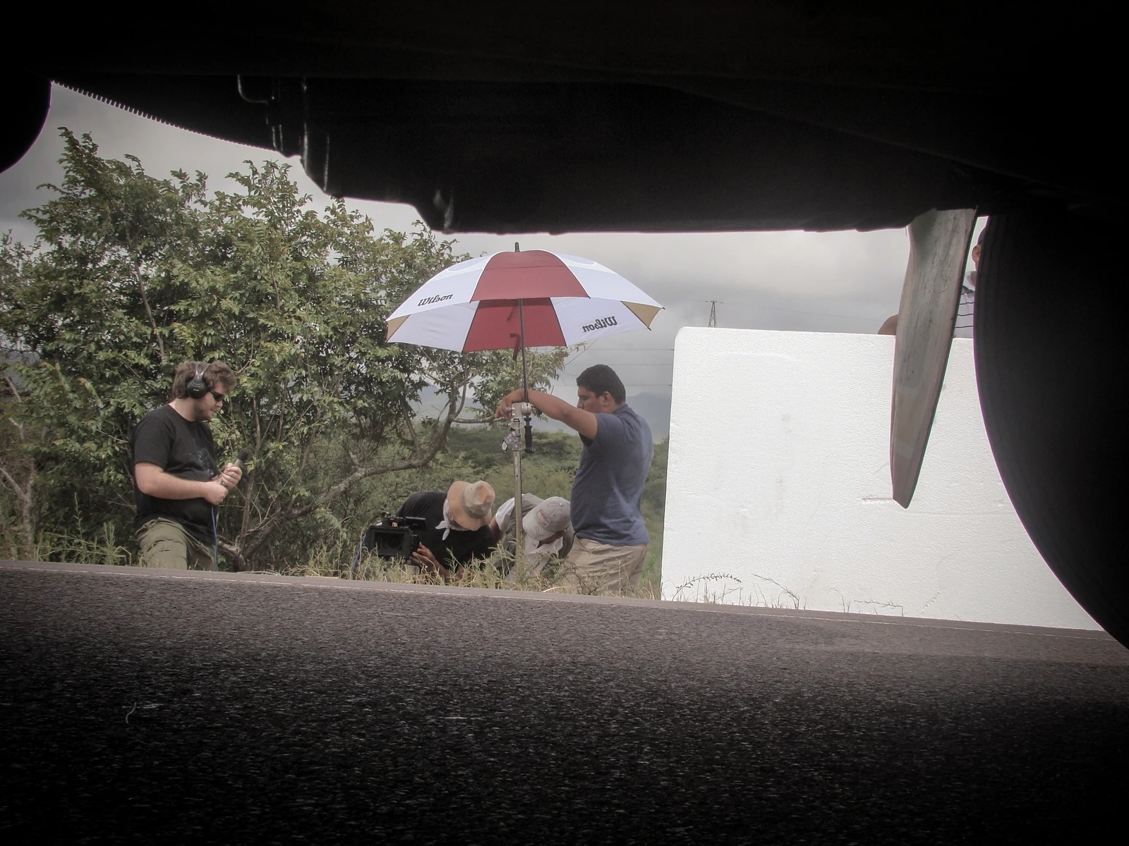 Equipo de rodaje visto desde debajo de un vehículo, con cámara y reflector